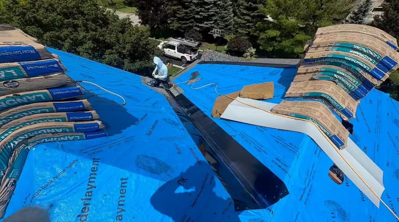 Black open metal valley flashing laid down a roof valley over blue synthetic underlayment, with CertainTeed Landmark shingle bundles staged in Stouffville