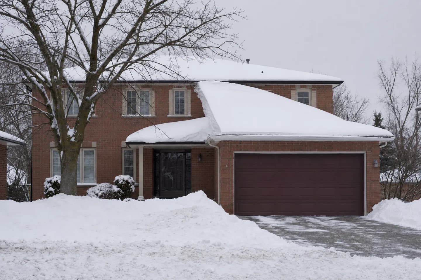 Snow drifted deep on the lower garage roof against the taller brick wall of a two-storey house in Newmarket, with an even layer on the main roof