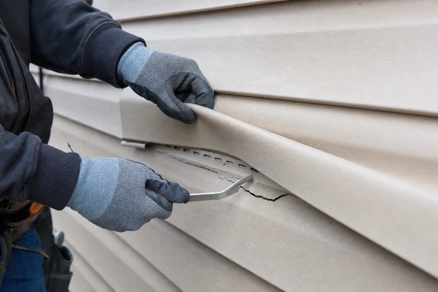 A siding installer uses a zip tool to unhook the course of vinyl siding above a cracked panel before replacing it