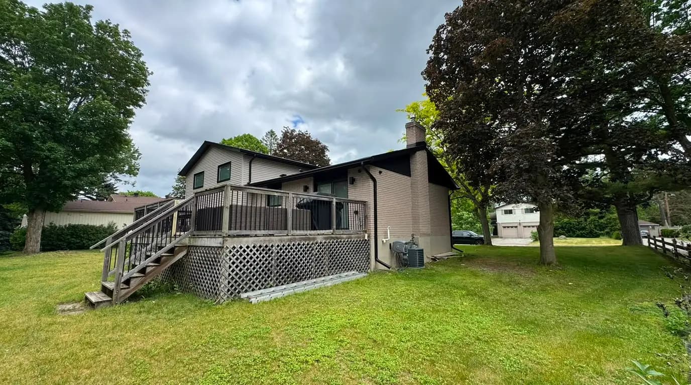 Wider view of the house before the reclad, showing the original dark gable and the lawn running down from the deck