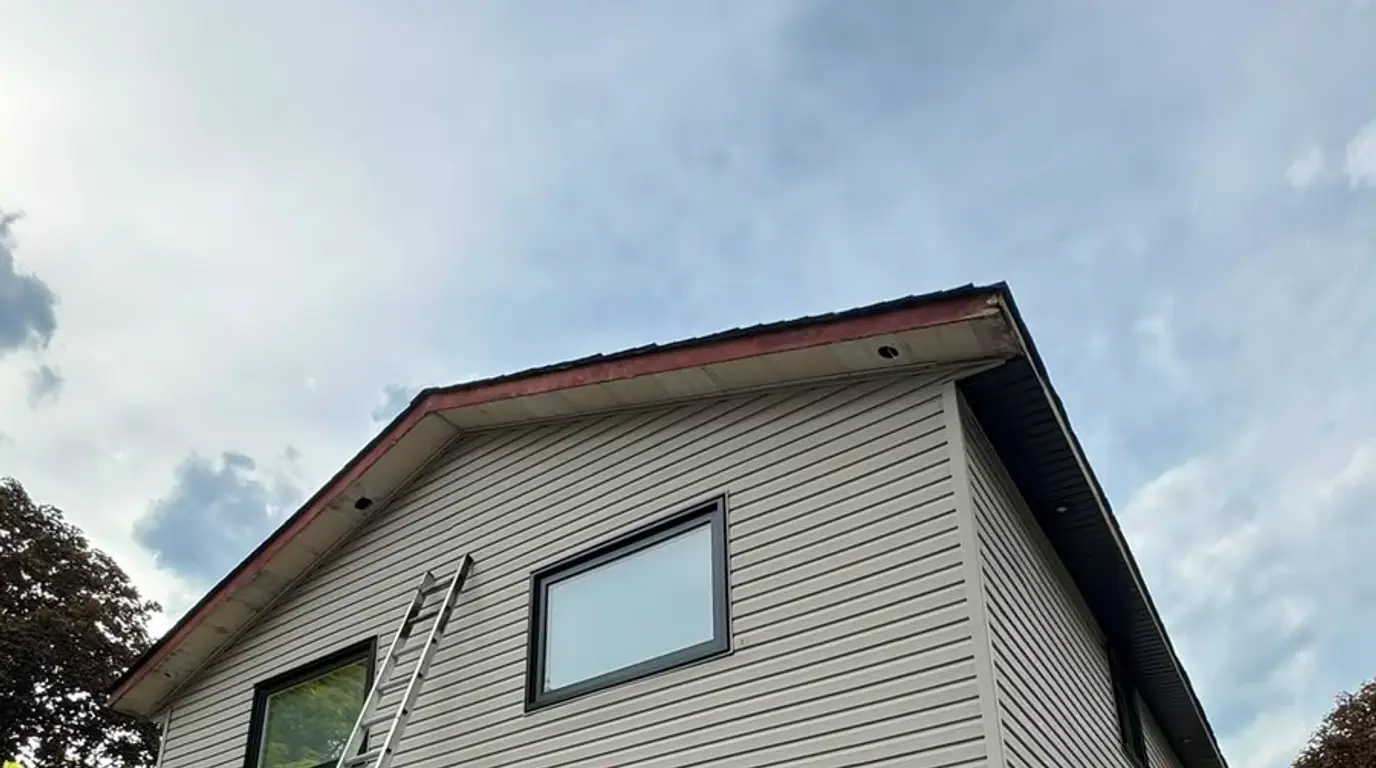 New siding going on above the garage with Typar building wrap still exposed over the sheathing, and a ladder against the upper storey