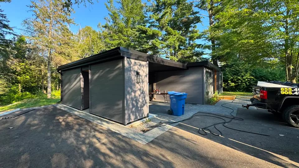 Detached garage and carport clad in dark plank siding with a black eavestrough along the low slope roof