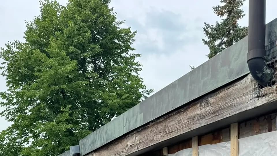 Installer fastening a course of dark plank siding over housewrap and vertical furring strips on a Toronto home