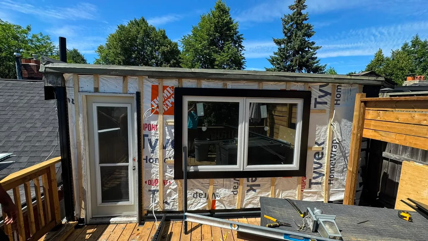 The same deck wall wrapped in Tyvek HomeWrap with the window and door framed out, before the new siding went on