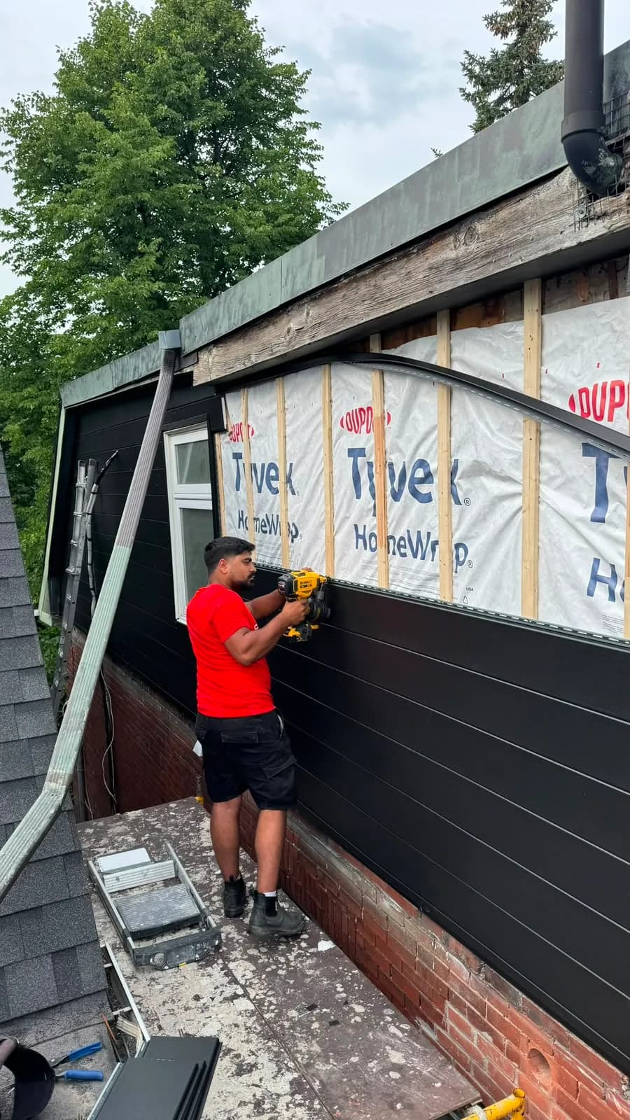 Sherak crew member fastening black horizontal siding to vertical wood strapping over Tyvek HomeWrap