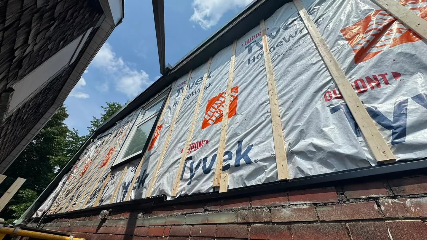 Upper wall wrapped and strapped, seen from below at the eave, with the strapping running top to bottom over the wrap
