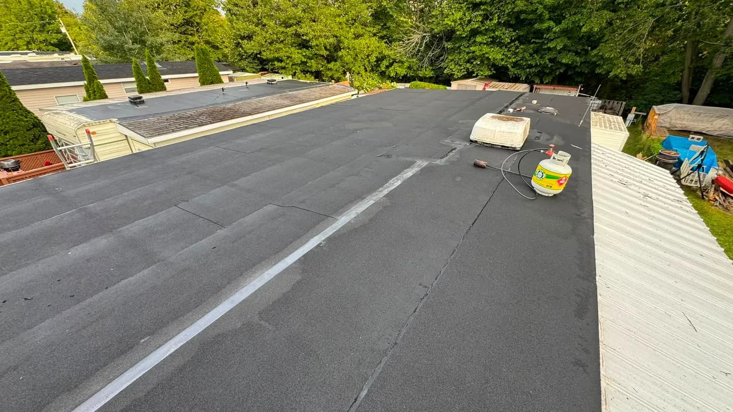 New membrane running the length of the roof near the end of the job, with the rooftop air conditioner and a propane cylinder still on the deck
