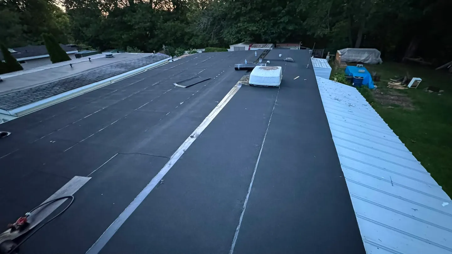 Long view down the finished flat roof at dusk, the laps of each membrane course visible across the surface