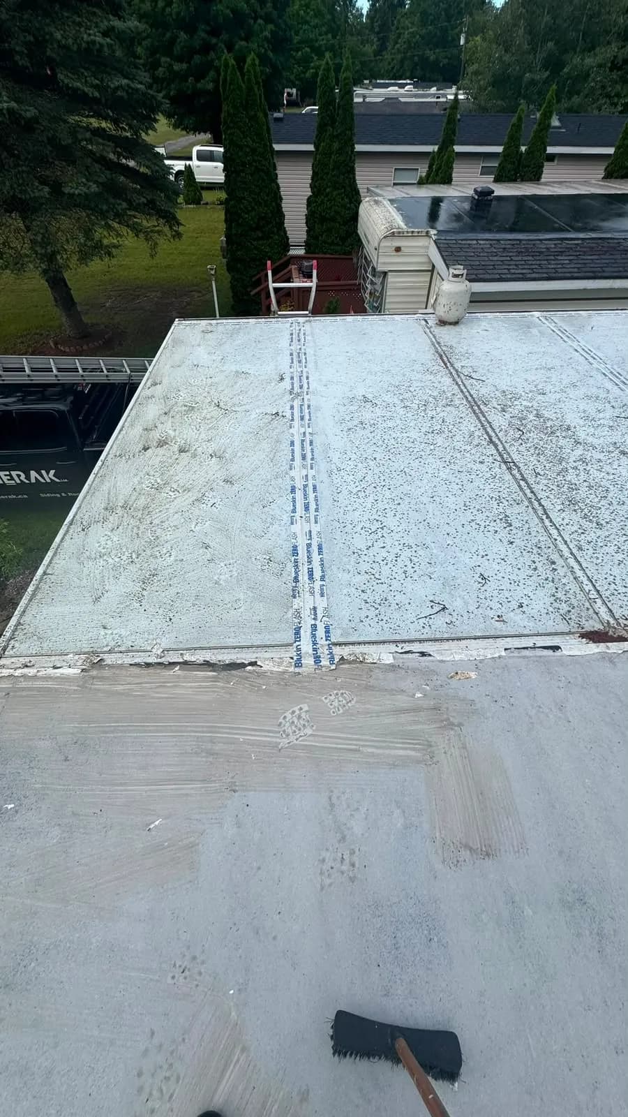 Old roof seams taped with self-adhered flashing tape before priming, with the Sherak truck parked below