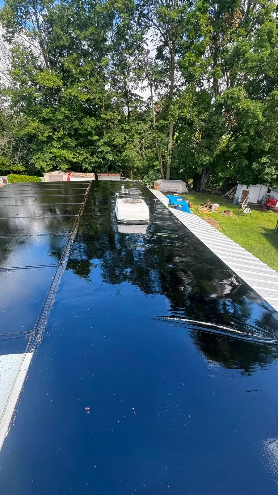 Glossy black primer coat over the whole roof, reflecting the trees, before the membrane went down