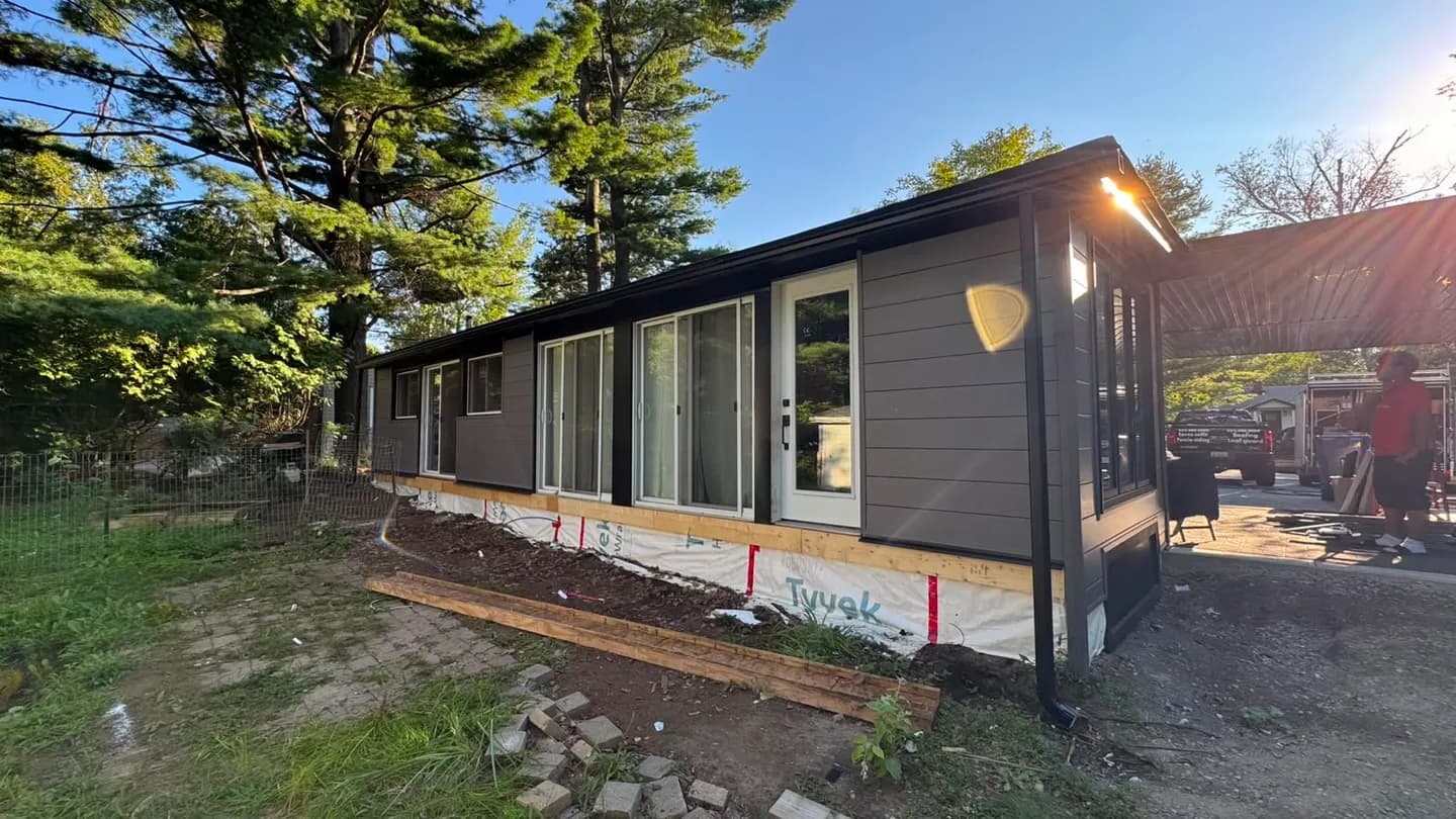 Rear elevation at dusk with the new siding partway along and Tyvek still showing at the base of the wall