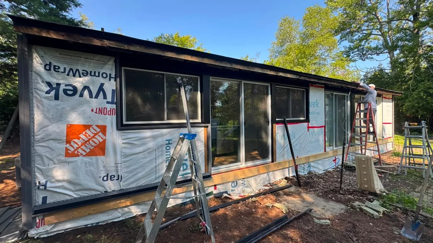 Rear wall wrapped in Tyvek HomeWrap with the window openings framed out and ladders against the eave