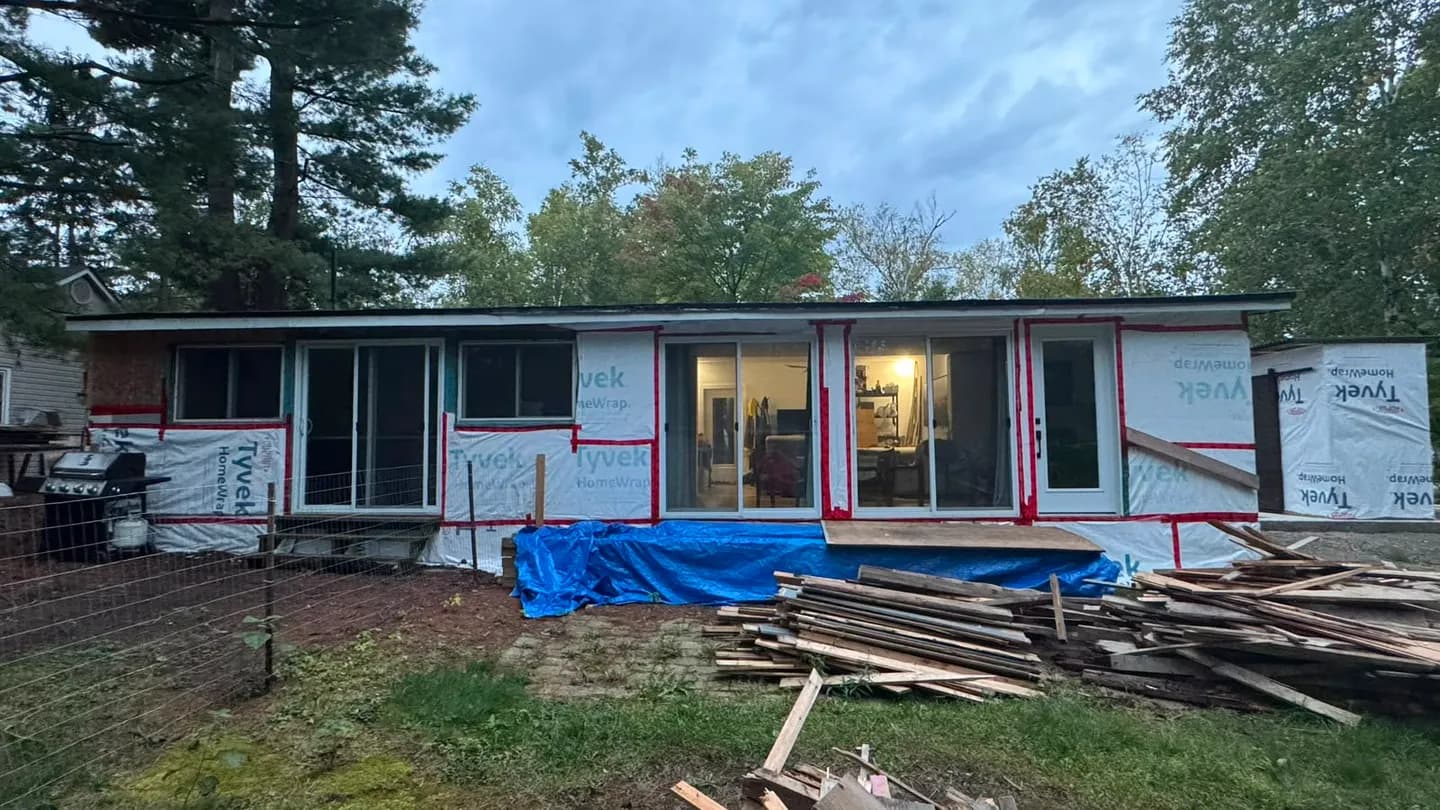 The whole rear of the house wrapped before the siding, with old lumber stacked on the lawn