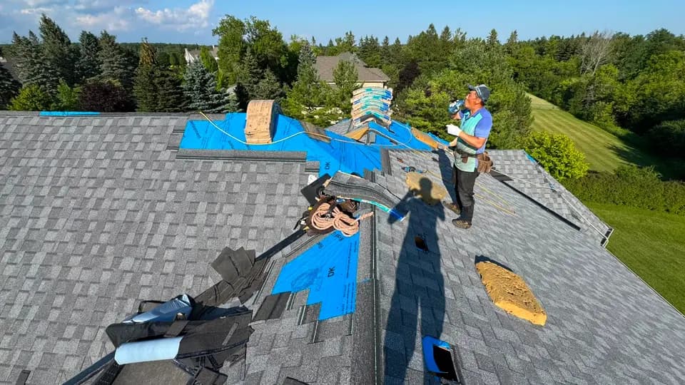 Sherak crew member laying shingle bundles over blue synthetic underlayment on a Stouffville roof