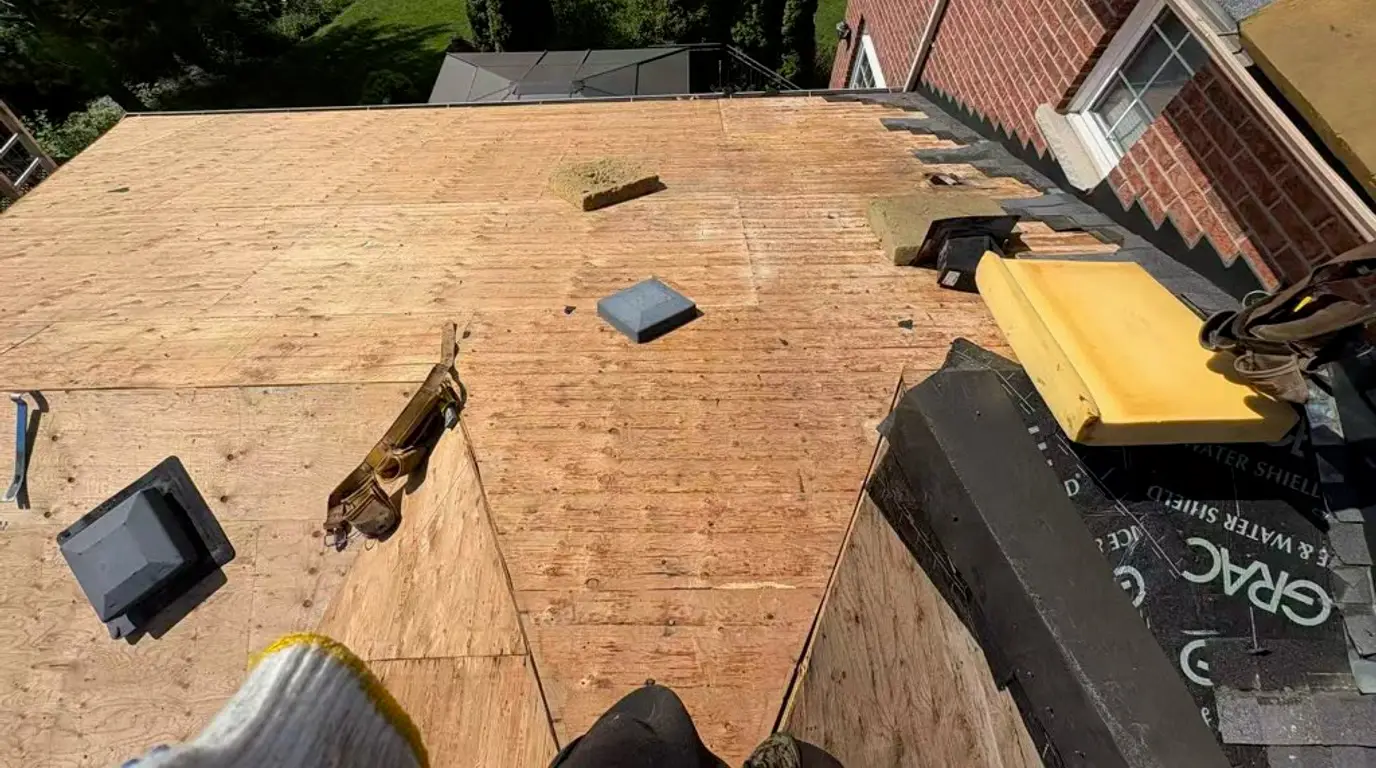 New plywood sheathing on the low slope section, with a roll of Grace Ice and Water Shield and the old step flashing stripped off the brick wall