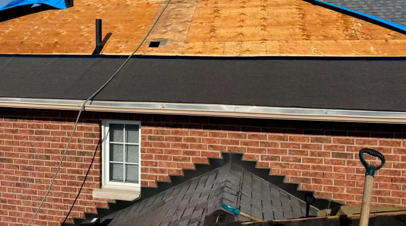 Sherak crew member working on the stripped roof of the brick house, with the old shingles cut back to the bare deck