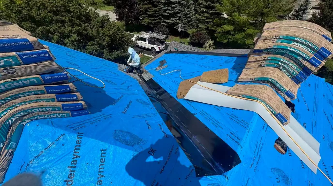 CertainTeed Landmark shingle bundles staged across the blue underlayment, with black open metal valley flashing run down the valley