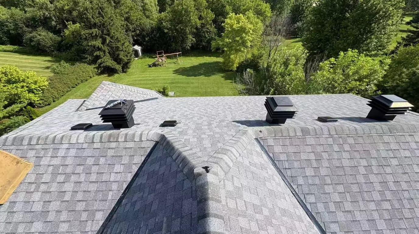 Completed shingle roof from the ridge, with low profile box vents set into the field and mature trees on the property