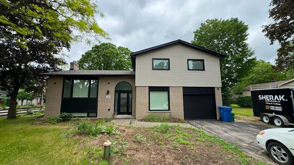 Front elevation of a brick side-split in Bradford with new taupe siding, black soffit, fascia and eavestrough, and the Sherak trailer at the curb
